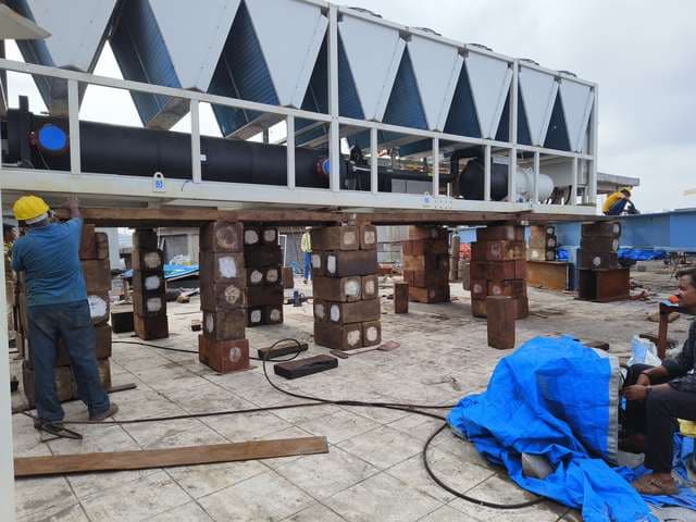 Air-cooled chiller supported on stacked timber cribbing on a terrace slab.