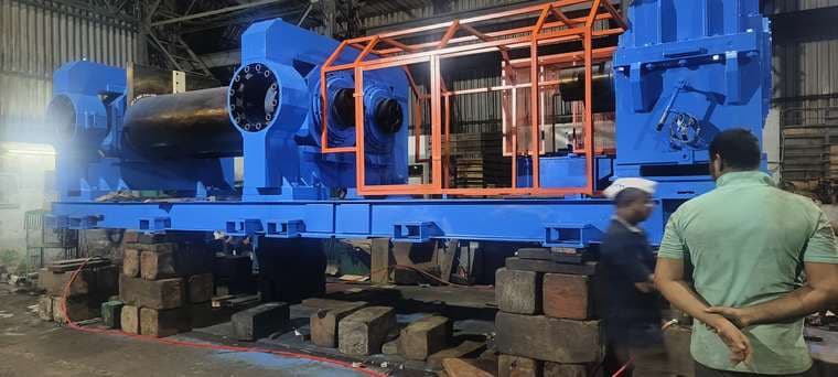 Large blue mill drive line supported on timber cribbing inside a fabrication shed.