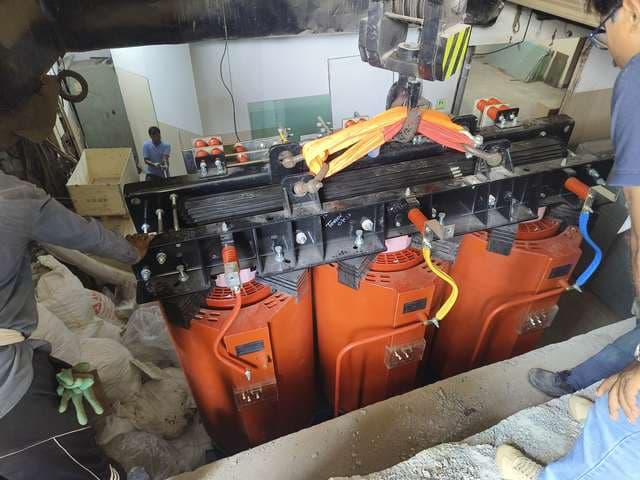 Dry-type transformer being lowered into a floor trench inside a building.