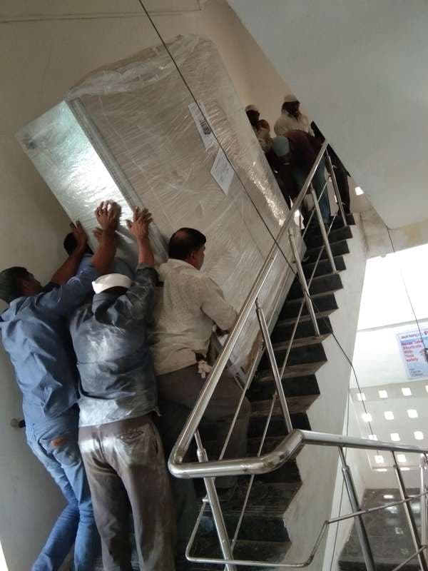 Riggers carrying a wrapped electrical panel by hand up a building stairwell.